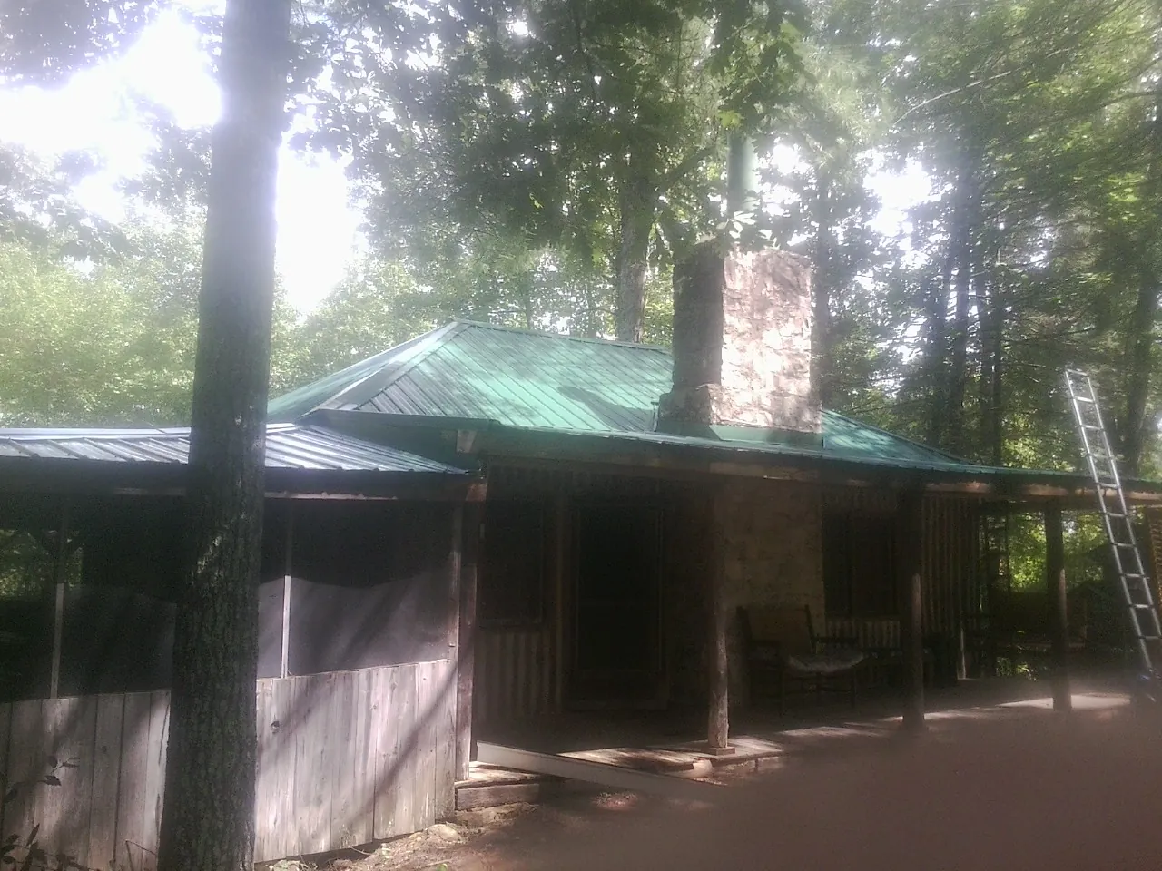 Green metal roof and stone chimney above a log cabin porch in Palmer