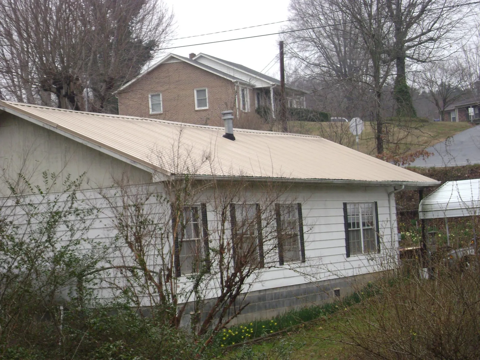 Tan metal roof on a white sided house set into a hillside — Commercial Roofing by Roofing Brothers in Palmer